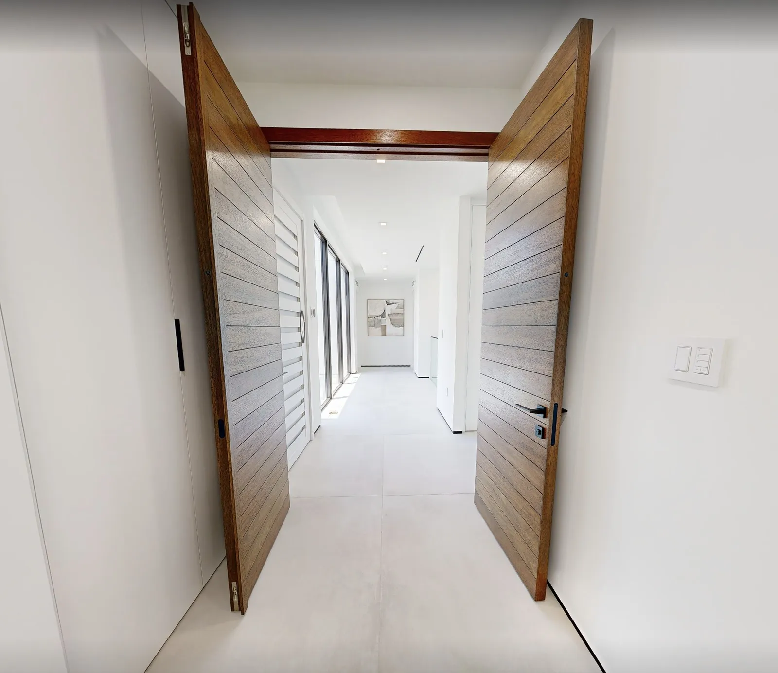 Wooden pivot doors opening onto a bright hallway in a modern luxury home in Miami, from one of our tours